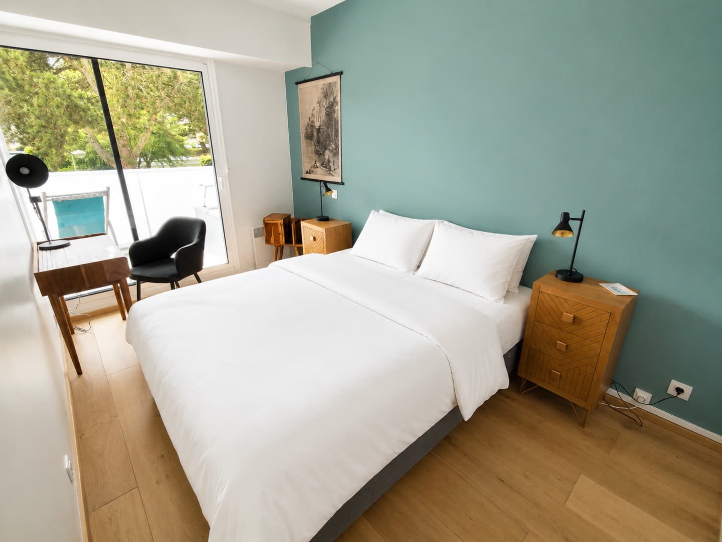 Chambre préparée : lit fait de linge blanc, mur vert d’eau, chevets en bois et lampes noires, vue sur les arbres