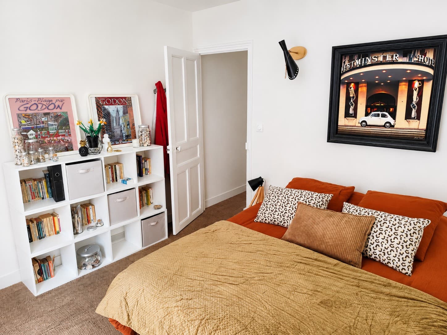 Chambre au linge orangé et coussins imprimés, bibliothèque blanche, affiches illustrées de Paris-Plage et grand cadre au mur