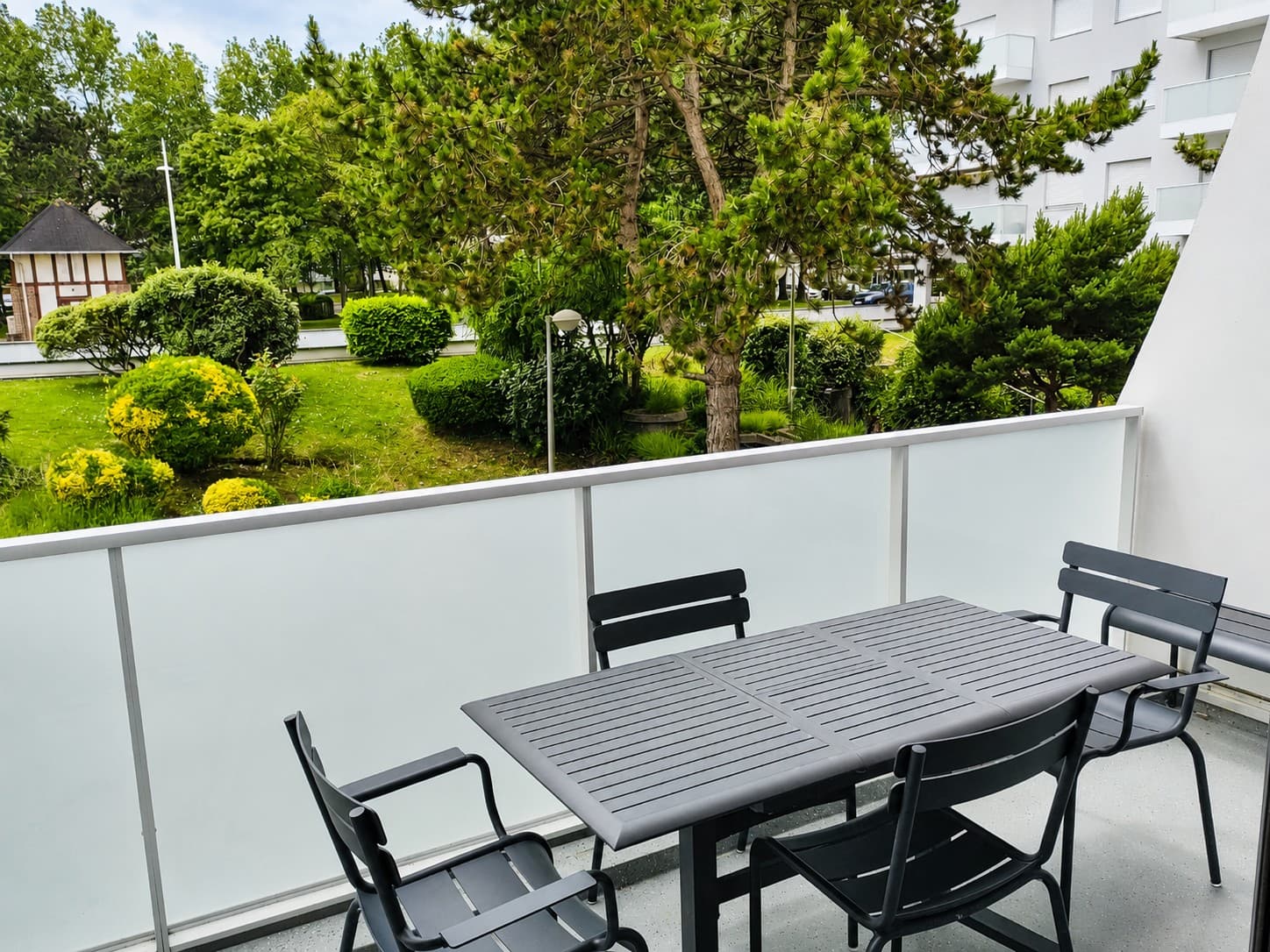Terrasse meublée d’une table et de chaises gris anthracite, ouverte sur un jardin planté de pins et d’arbustes fleuris