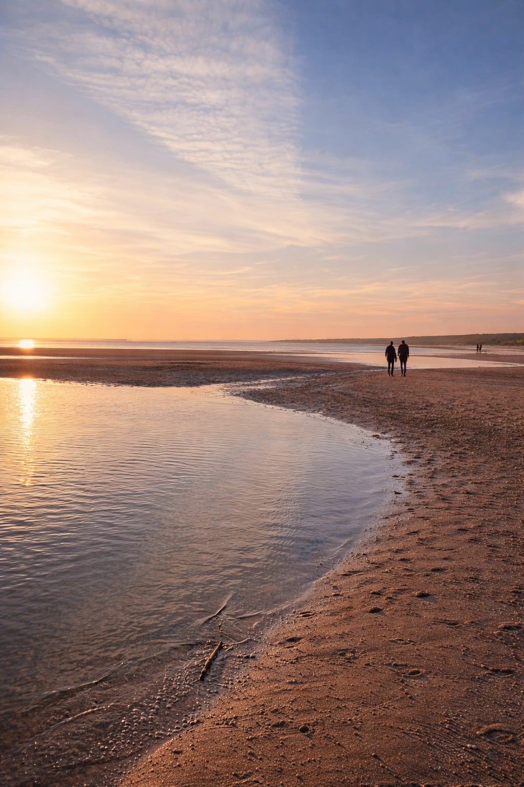 Plage à marée basse au coucher du soleil : le ciel se reflète dans une nappe d’eau, deux promeneurs marchent au loin sur le sable