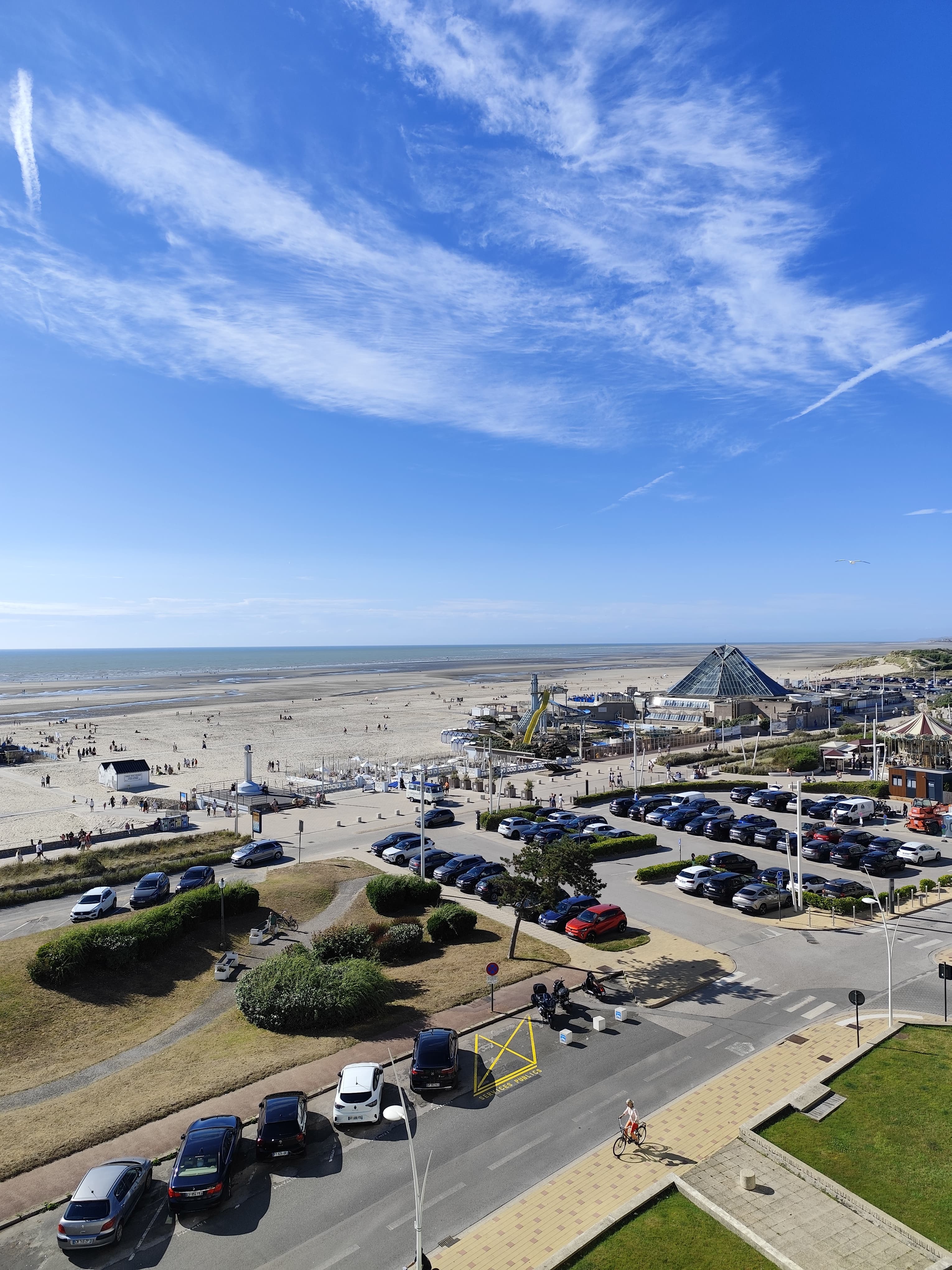 Vue en hauteur sur la grande plage à marée basse et le front de mer, sous un ciel bleu traversé de nuages légers