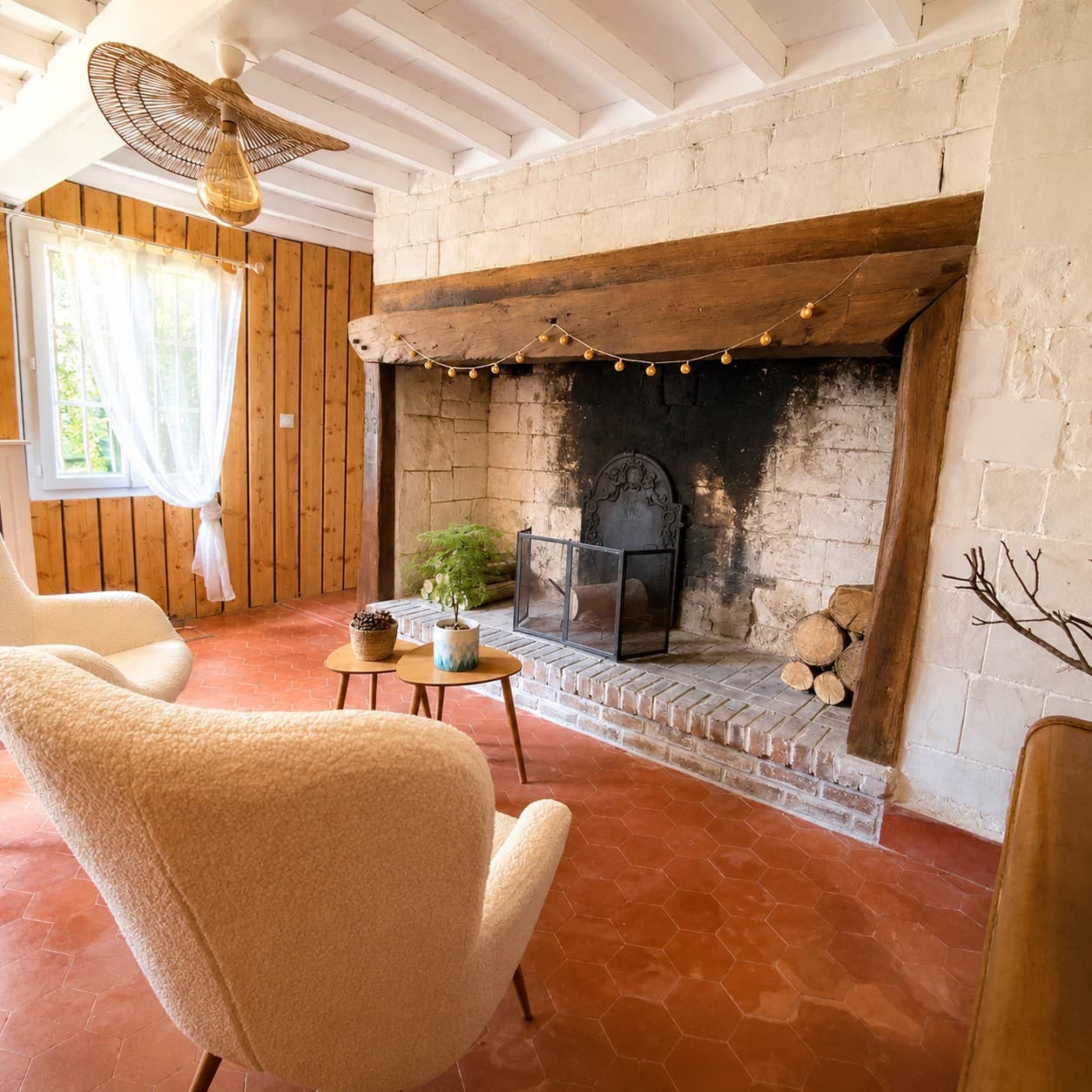 Intérieur de caractère avec grande cheminée de pierre, poutres, fauteuil et sol en terre cuite